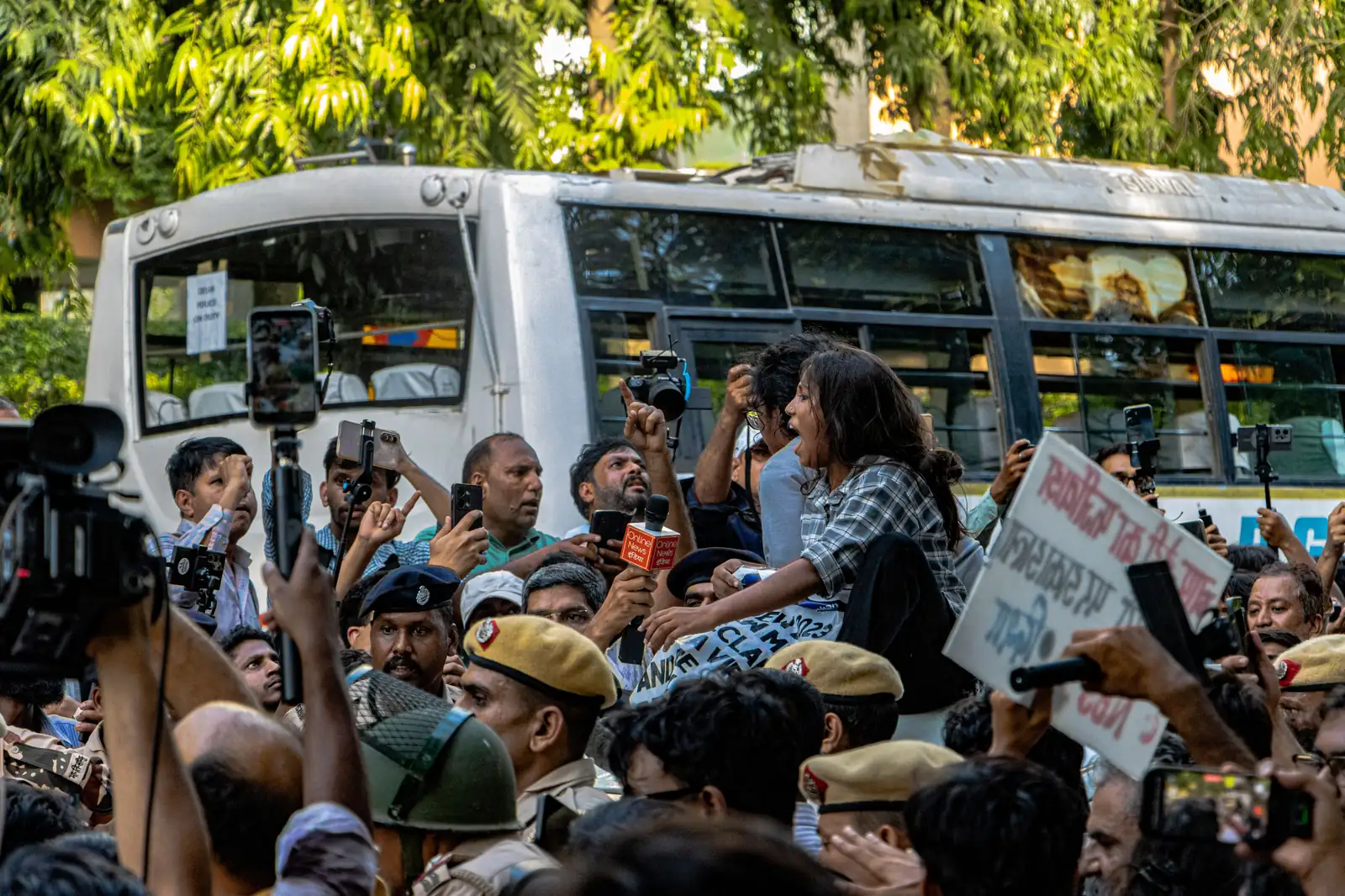 Protesters, police and media crowd around a police bus in Delhi